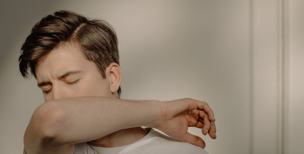 Person som verkar vara förkyld och nyser i armvecket.