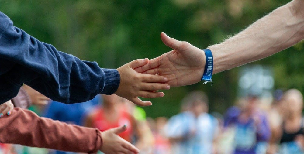 Händer som möts. I bakgrunden syns färgklädda människor.