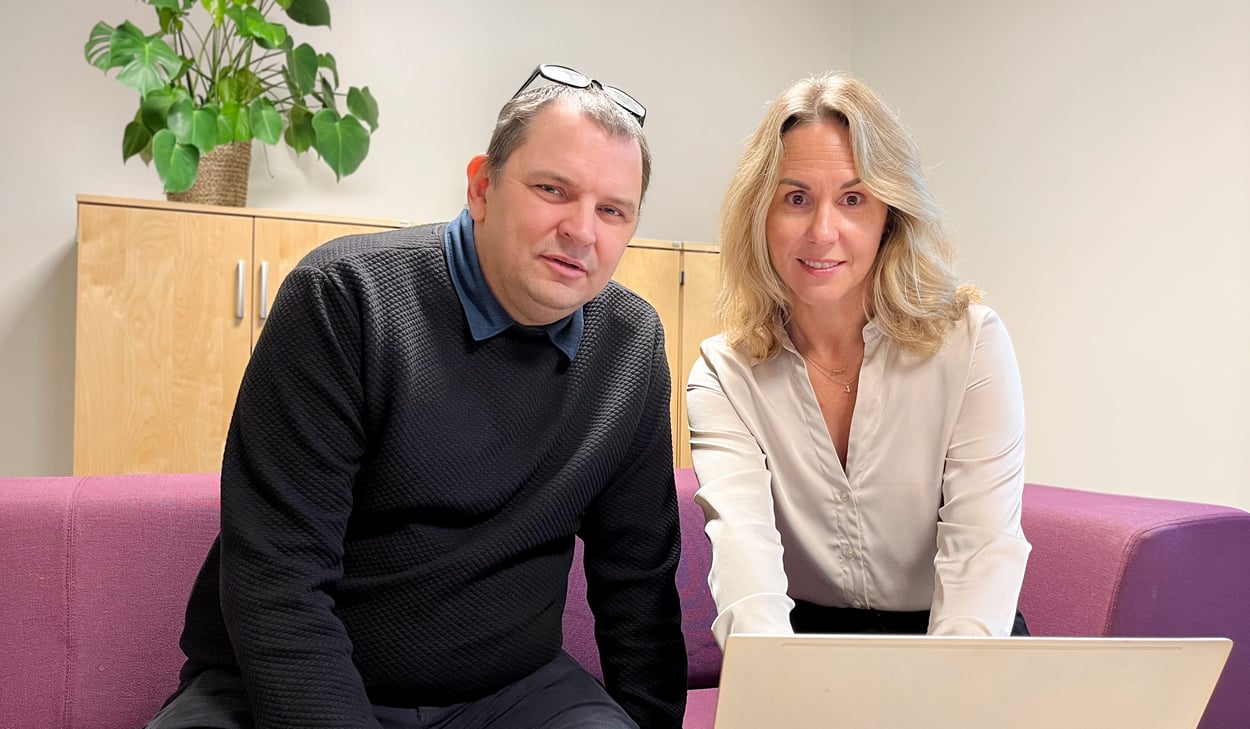 Sam Cole och Malin Schönning sitter i en vinröd soffa med en dator framför sig på ett bord. 