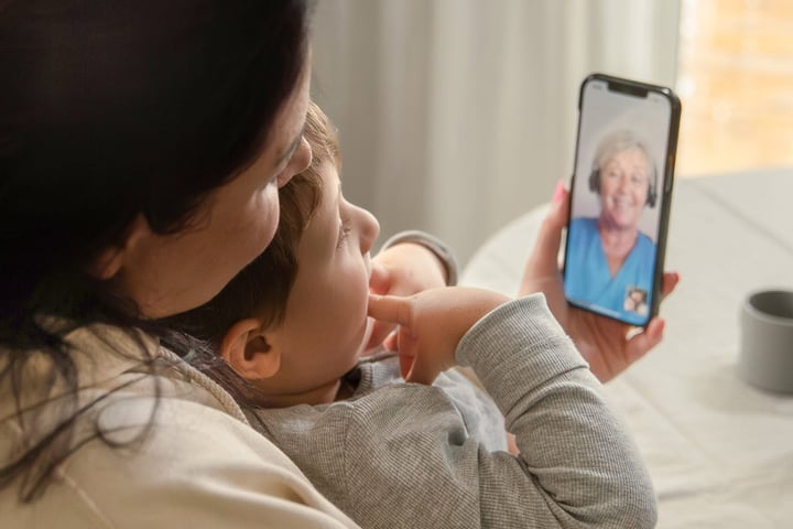 Barn som sitter i kvinnas famn. Pratar med Min vård Gävleborg i telefon.